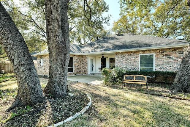 single story home with a ceiling fan, a front yard, a shingled roof, brick siding, and a patio area