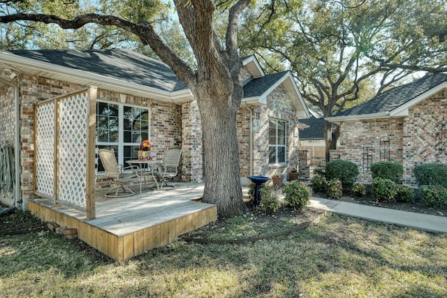 view of side of property with a deck, brick siding, and a shingled roof