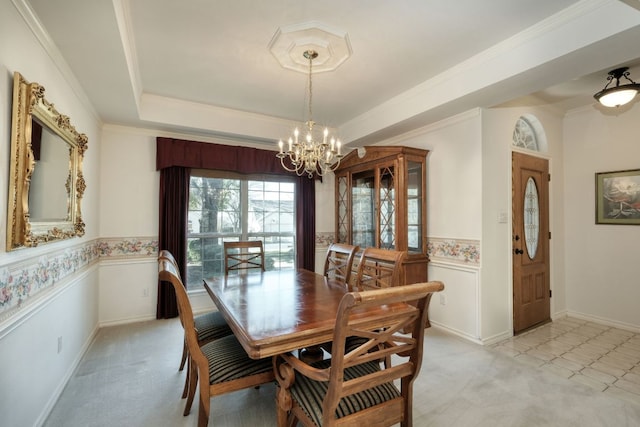 dining area with a wainscoted wall, light carpet, a notable chandelier, crown molding, and a raised ceiling