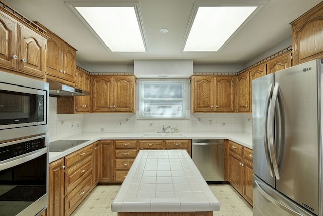 kitchen with under cabinet range hood, stainless steel appliances, light floors, and a sink