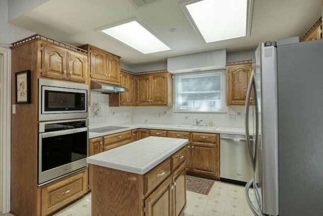 kitchen with light floors, a sink, stainless steel appliances, under cabinet range hood, and brown cabinets