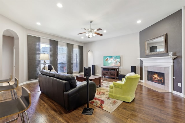 living room featuring arched walkways, wood finished floors, a ceiling fan, and a tile fireplace