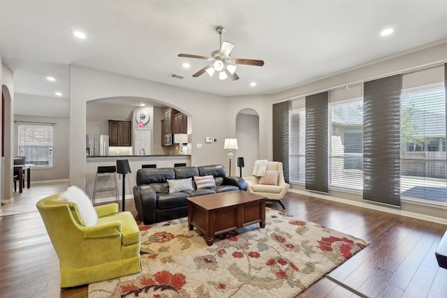 living area featuring arched walkways, a healthy amount of sunlight, and light wood-type flooring