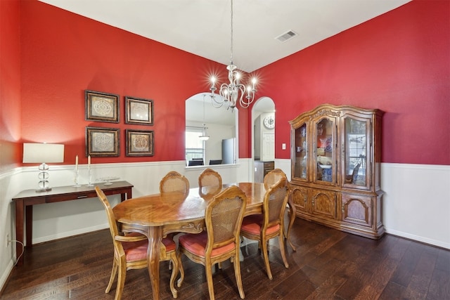 dining space featuring hardwood / wood-style floors, visible vents, an inviting chandelier, arched walkways, and wainscoting