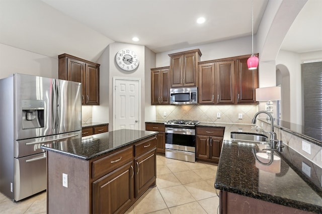 kitchen with backsplash, dark stone countertops, arched walkways, stainless steel appliances, and a sink