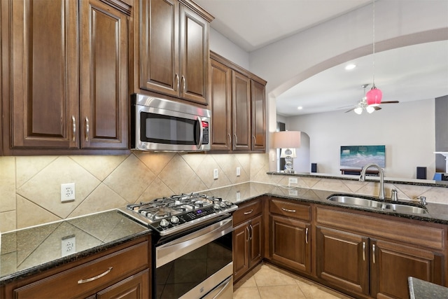 kitchen featuring a ceiling fan, dark stone counters, arched walkways, a sink, and stainless steel appliances