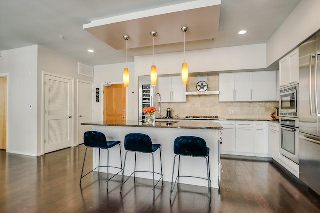 kitchen with wall chimney range hood, a breakfast bar area, decorative backsplash, appliances with stainless steel finishes, and a sink