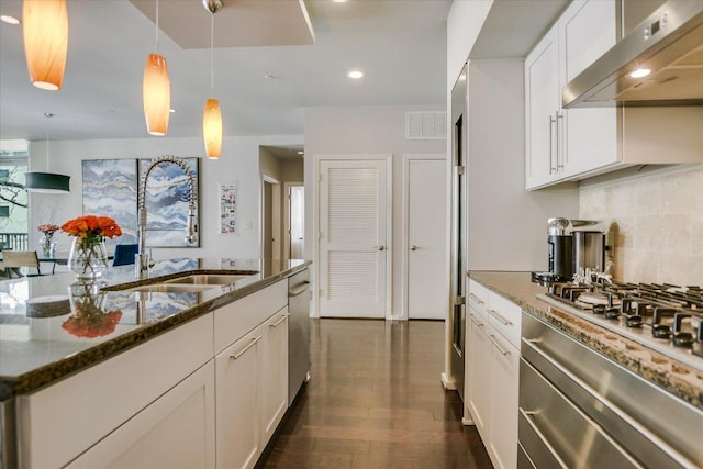 kitchen with a sink, backsplash, dark wood-style floors, dark stone counters, and extractor fan