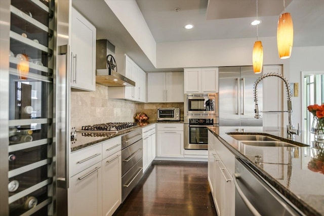 kitchen featuring a sink, stainless steel appliances, dark stone counters, and wall chimney range hood