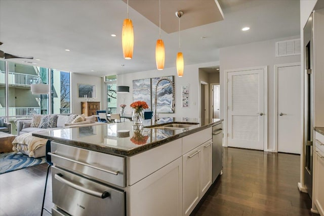 kitchen featuring visible vents, dark wood finished floors, open floor plan, dark stone counters, and stainless steel dishwasher