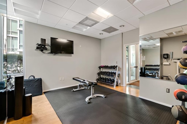 exercise room with baseboards, a paneled ceiling, and wood finished floors