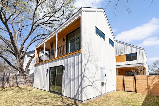 back of house with a balcony, a fenced backyard, board and batten siding, and a lawn