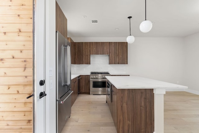 kitchen with high end appliances, light wood finished floors, decorative backsplash, modern cabinets, and a center island