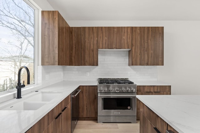 kitchen with modern cabinets, a sink, light stone counters, stainless steel appliances, and decorative backsplash