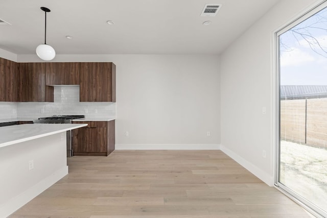 kitchen with high end range, visible vents, light countertops, light wood-style floors, and tasteful backsplash