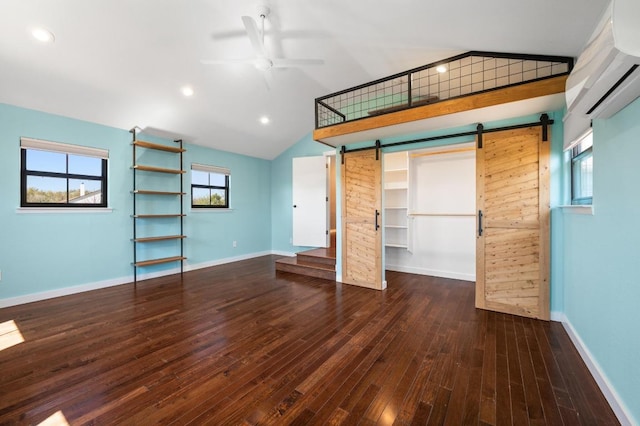 interior space featuring a wall unit AC, lofted ceiling, a barn door, and hardwood / wood-style floors