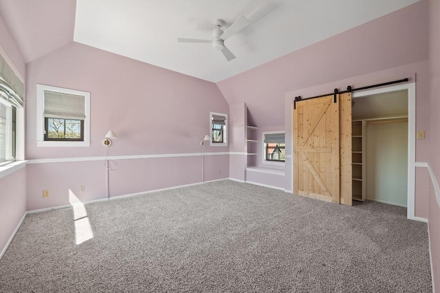 spare room featuring ceiling fan, baseboards, carpet, a barn door, and lofted ceiling