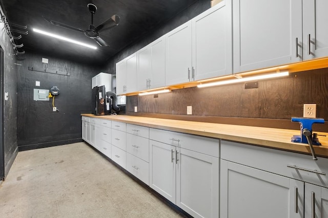 kitchen featuring white cabinets, a ceiling fan, concrete flooring, and wood counters