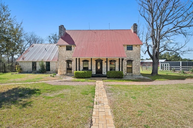 view of front of home with stone siding, a chimney, a front yard, and metal roof