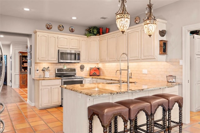 kitchen with visible vents, a breakfast bar, a sink, appliances with stainless steel finishes, and light stone countertops