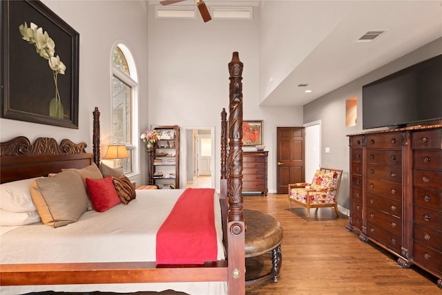 bedroom with visible vents, ensuite bathroom, a towering ceiling, and wood finished floors