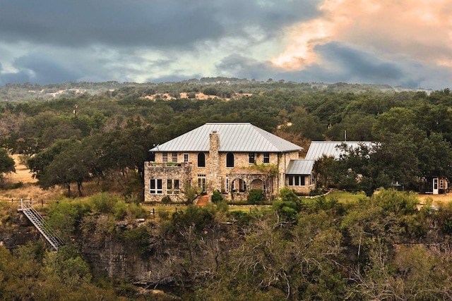 rear view of property featuring a forest view, metal roof, a standing seam roof, and stone siding