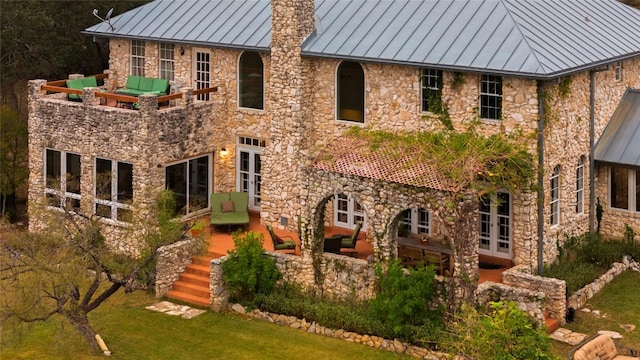 rear view of house featuring an outdoor living space, a lawn, metal roof, stone siding, and a standing seam roof