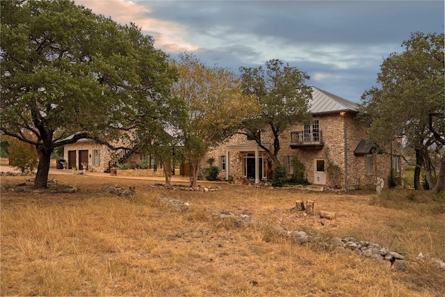 view of front of house featuring a standing seam roof, a balcony, stone siding, and metal roof