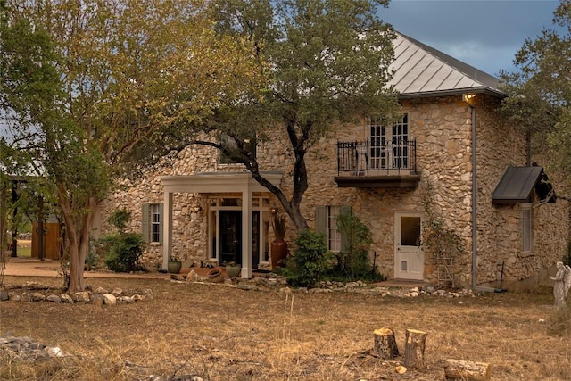 rear view of property with stone siding, a balcony, metal roof, and a standing seam roof