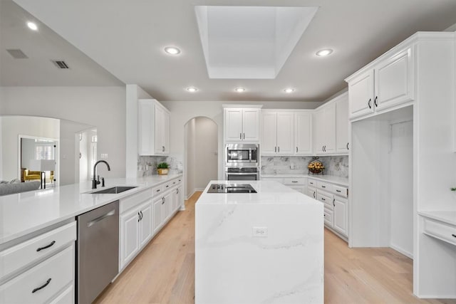 kitchen featuring light wood finished floors, recessed lighting, arched walkways, stainless steel appliances, and a sink