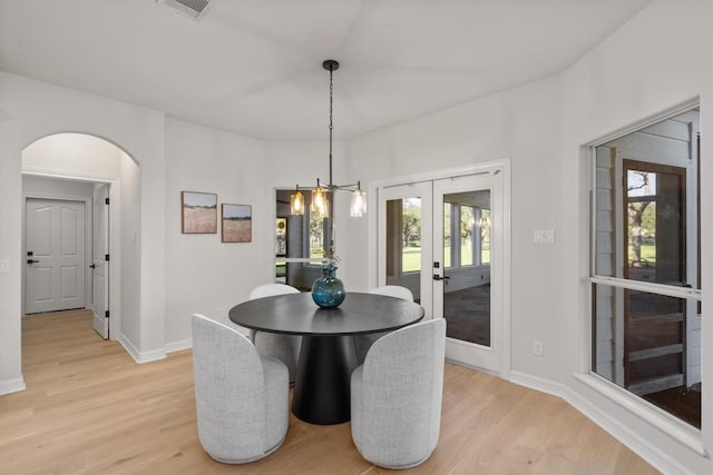 dining space featuring arched walkways, french doors, light wood-type flooring, and baseboards