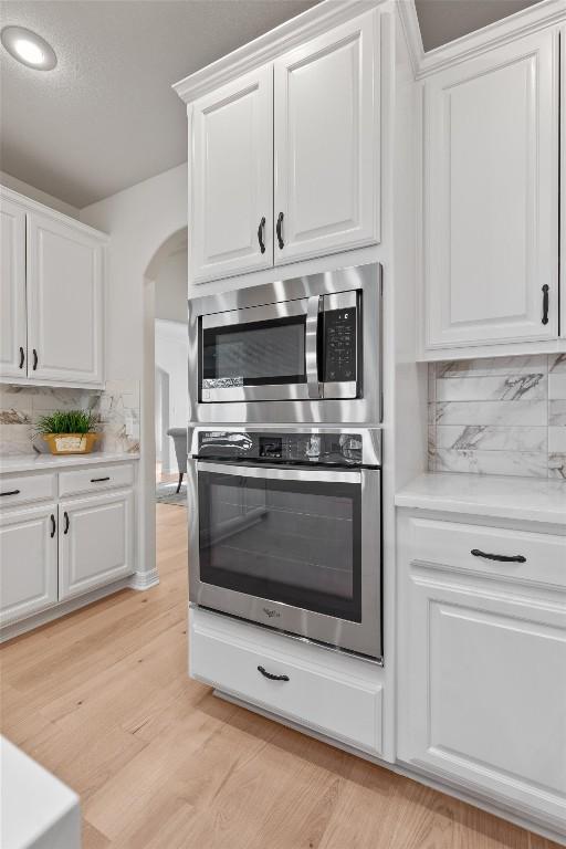 kitchen with arched walkways, appliances with stainless steel finishes, white cabinets, and light wood finished floors