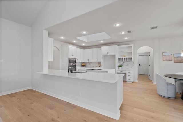 kitchen featuring a peninsula, arched walkways, a sink, light wood-style floors, and stainless steel microwave