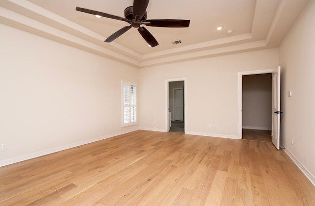 spare room featuring visible vents, baseboards, ceiling fan, light wood-style floors, and a raised ceiling