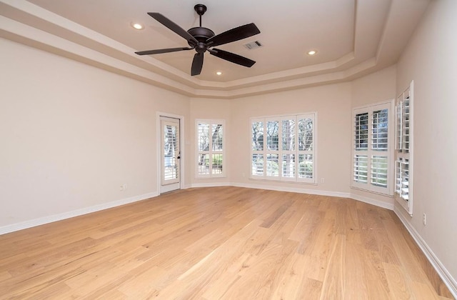 empty room with visible vents, a tray ceiling, recessed lighting, light wood finished floors, and baseboards