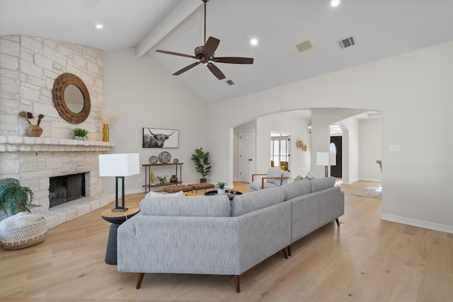 living area featuring light wood finished floors, visible vents, beam ceiling, arched walkways, and a ceiling fan