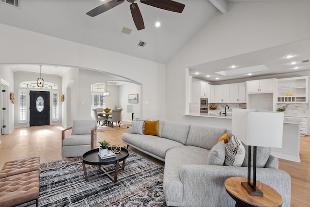 living room featuring beam ceiling, high vaulted ceiling, light wood-style flooring, arched walkways, and ceiling fan