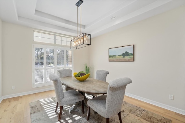 dining room featuring a notable chandelier, a raised ceiling, light wood-style floors, and baseboards