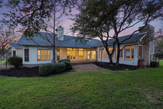 back of house at dusk with a chimney, a yard, and fence