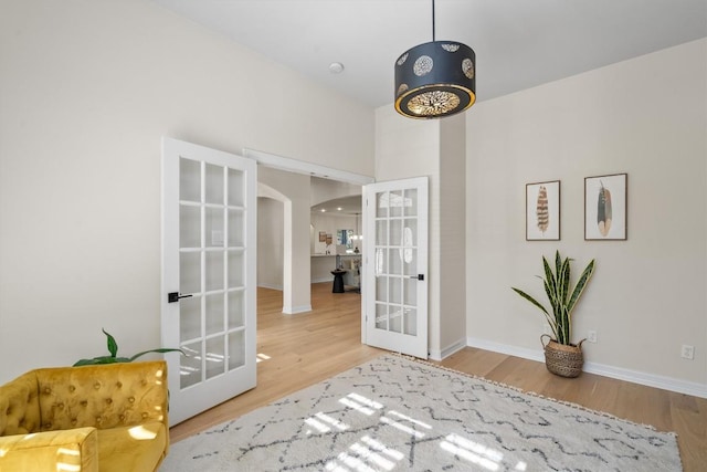 doorway with french doors, arched walkways, baseboards, and wood finished floors