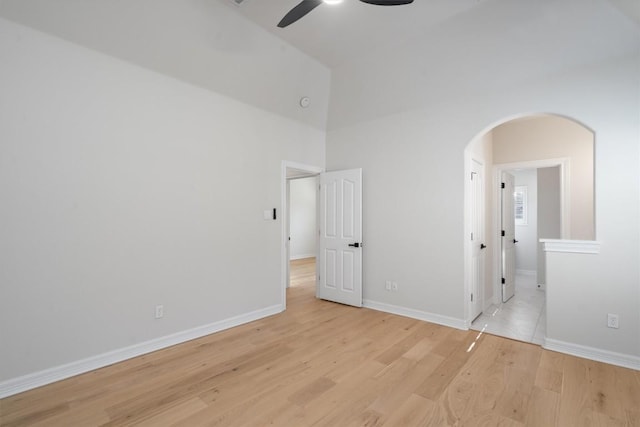 unfurnished bedroom with light wood finished floors, baseboards, ensuite bathroom, a high ceiling, and arched walkways