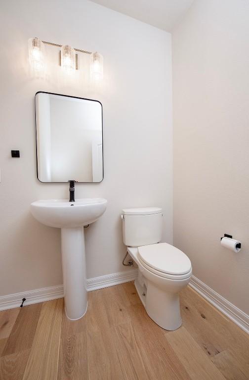 half bathroom featuring baseboards, toilet, and wood finished floors