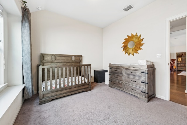 bedroom with a crib, vaulted ceiling, carpet flooring, and visible vents