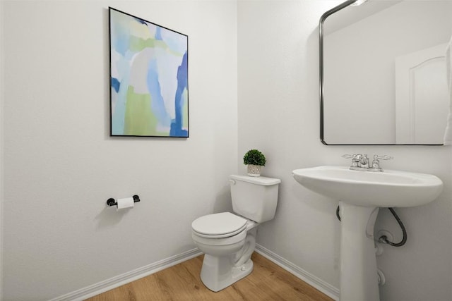 half bathroom with toilet, baseboards, and wood finished floors