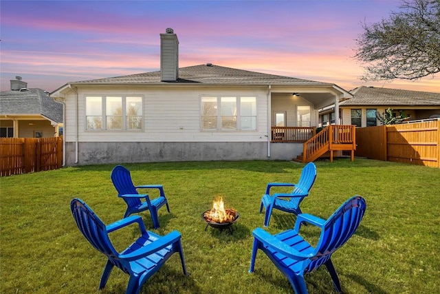 back of house at dusk featuring a chimney, a yard, a fire pit, and a fenced backyard