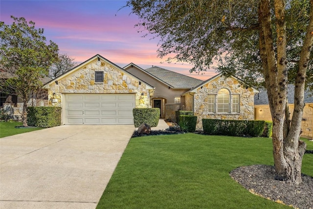 french country style house with stone siding, a garage, driveway, and a yard