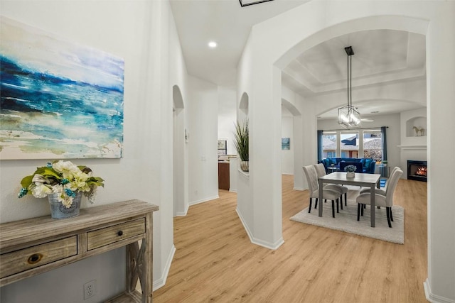 interior space featuring light wood finished floors, baseboards, recessed lighting, a warm lit fireplace, and arched walkways