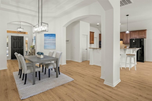 dining room featuring visible vents, light wood finished floors, baseboards, an inviting chandelier, and arched walkways