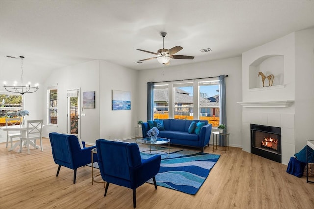 living area featuring ceiling fan with notable chandelier, wood finished floors, visible vents, and a tile fireplace