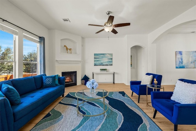 living area with visible vents, ceiling fan, a lit fireplace, wood finished floors, and arched walkways